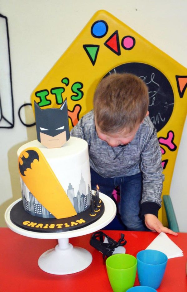 Birthday boy blowing out his Batman cake candles